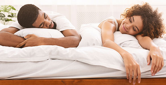 Man and woman lying on their stomach on bed, looking at each other