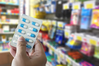 Hand holding a blister pack of blue and white capsules. Background is a blurred convenience store