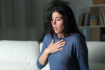 Dark haired woman with her hand on her chest looking like she is anxious