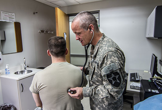 Service member doctor listening to the lungs of a service member with a stethoscope