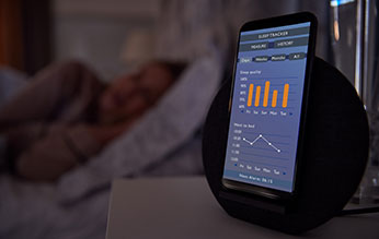 Woman in bed sleeping in background, in foreground a mobile phone with an open sleep app