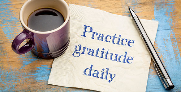 Coffee cup on table with a napkin sitting next to it. The napkin has writing that says Practice gratitude daily