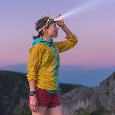 Woman standing on a hill at sunset adjusting her headlamp