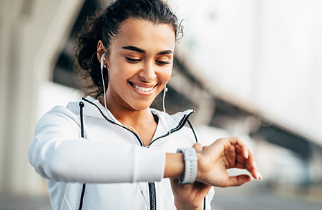 A smiling woman is looking at her sportwatch as she prepares to do exercise