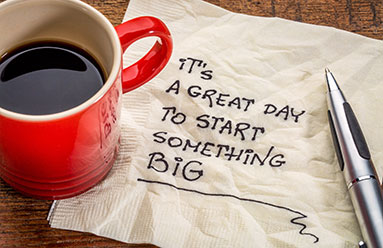 Note on a napkin next to a red cup of coffee. The note reads It's a great day to start someting big!