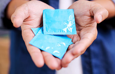 Close up of a man's hands holding 3 condoms in his palms