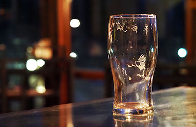 An empty beer glass sitting on a bar, with suds still inside the glass