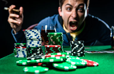 A man sitting behind poker chips with a glass of wine and a cigar. The man appears to be overstimulated